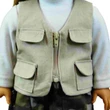 A close-up shot of an 18-inch doll wearing a tan, zippered utility fishing vest over a light gray or white long-sleeve shirt. The doll-sized vest features a functional silver zipper down the center and four small pockets with rounded flaps—two on the chest and two near the waist. The top of camouflage-patterned pants is visible at the bottom of the frame.