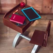 A high-angle view shows a miniature vintage-style school desk and attached chair set arranged on a light wood floor. The brown wooden desktop holds a toy slate board with a bright blue border, a red "HISTORY" book stacked over a green book, a short yellow pencil, and a red apple model. The matching wooden chair seat sits empty, connected to the main desk by a metallic silver painted frame.