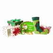 A miniature holiday accessory set is arranged in a cluster against a solid white background. The collection includes a white gift box with red polka dots and a red bow shown half-open, a green striped square gift box with a green bow, and a small red gift box with a white ribbon. In the center, a green oval plate reading "Cookies for Santa" stands upright next to two toy cookies, a tiny green mug labeled "MILK", and a curved green elf stocking with red pom-poms.