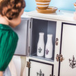 In kitchen play scene, an 18 inch doll has opened a door of our 1930s white icebox to take out one bottle of milk. In kitchen play scene, an 18 inch doll has opened a door of our 1930s white icebox to take out one bottle of milk.