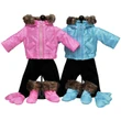 Two doll winter outfits are displayed side-by-side on black stands against a white background, featuring a bright pink hooded jacket on the left and a light blue one on the right, both paired with black pants, matching fur-trimmed boots, and mittens.