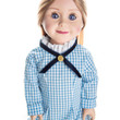 A close-up portrait of a pioneer doll with blue eyes and brown hair wearing a blue and white checkered gingham dress with a blue cross-ribbon collar on a white background.