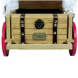 A close-up view of an open miniature wooden doll trunk featuring dark faux-leather straps with gold studs, an ornate black central emblem, and a metal plaque against a white background.
