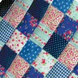 A close-up view of a doll patchwork quilt featuring alternating squares of blue polka dots, gingham, and floral patterns.