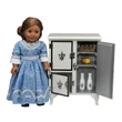 An 18-inch doll in a blue period-style dress stands beside a miniature white vintage icebox with an open side door revealing realistic toy food, including two milk bottles and cheese.