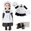 An 18-inch doll dressed in a historic kitchen maid uniform stands on the left against a solid white background. She wears a black long-sleeved dress, a ruffled white apron, a white mop cap, and dark brown lace-up boots. To the right, a second identical outfit is laid out flat, displaying a matching black dress, white apron, white mop cap, and white bloomers. A pair of miniature dark brown lace-up boots sits in the lower right corner next to a small white shoe box.