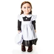 An 18-inch doll with brown hair in two low braided pigtails stands facing forward against a plain white background. She is wearing a historic kitchen maid outfit consisting of a black long-sleeved dress, a crisp white pinafore apron with ruffled shoulder straps, and dark brown leather-look boots. She holds a matching white fabric mop cap in her right hand down by her side.