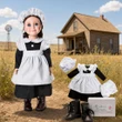 An 18-inch doll dressed in a historic kitchen maid uniform stands on the left against a solid white background. She wears a black long-sleeved dress, a ruffled white apron, a white mop cap, and dark brown lace-up boots. To the right, a second identical outfit is laid out flat, displaying a matching black dress, white apron, white mop cap, and white bloomers. A pair of miniature dark brown lace-up boots sits in the lower right corner next to a small white shoe box. The background is a prairie outdoor scene
