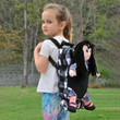 In outdoor scene, a child models the black and white checked backpack with Charlotte Rag Doll in the carrier pocket. In outdoor scene, a child models the black and white checked backpack with Charlotte Rag Doll in the carrier pocket.