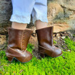 A close-up photograph shows an 18-inch doll wearing brown leather-style boots while standing outdoors.