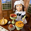 In kitchen setting, a scullery maid doll has our Apple and Pecan pies in pie stands and serving a slice of the pecan pie on silver dish and wooden mixing  bowl with spoon beside it. In kitchen setting, a scullery maid doll has our Apple and Pecan pies in pie stands and serving a slice of the pecan pie on silver dish and wooden mixing  bowl with spoon beside it.