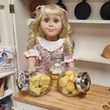 An 18-inch doll stands behind a wooden counter displaying miniature jars from the Little House on the Prairie® collection, filled with toy cheese, eggs, and biscuits.