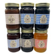 Six jars of Caroline's Kitchen fruit spreads arranged in two stacked rows, featuring flavors like Apple Butter, Black Raspberry Jam, Elderberry Jelly, and Damson Plum Jam, each with a distinctive gingham pattern label against a solid white background.