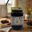 A jar of Grandma's Blackberry Jam by The Queens Treasures® sits on a rustic wooden table next to a biscuit spread with jam, a small bowl of fresh blackberries, and a vase of wildflowers.