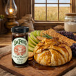 Dr. Pete's Praline Mustard Glaze jar on a rustic wood table in front of a  Golden baked puff pastry Brie topped with warm praline glaze on a charcuterie platter with fruit and crackers