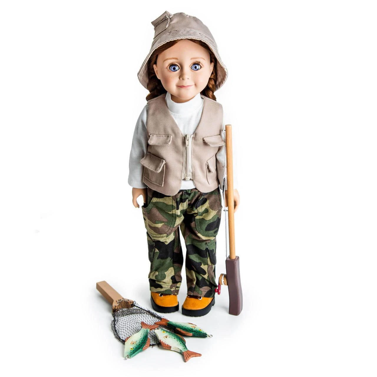 An 18-inch doll dressed in a complete fishing adventure outfit, standing against a solid white background. The doll wears a tan bucket hat, a tan utility vest over a white long-sleeve shirt, camouflage pants, and tan hiking boots with dark soles. The doll holds a wooden toy fishing pole in its left hand. At its feet rests a miniature wooden-handled fishnet containing three small toy fish.