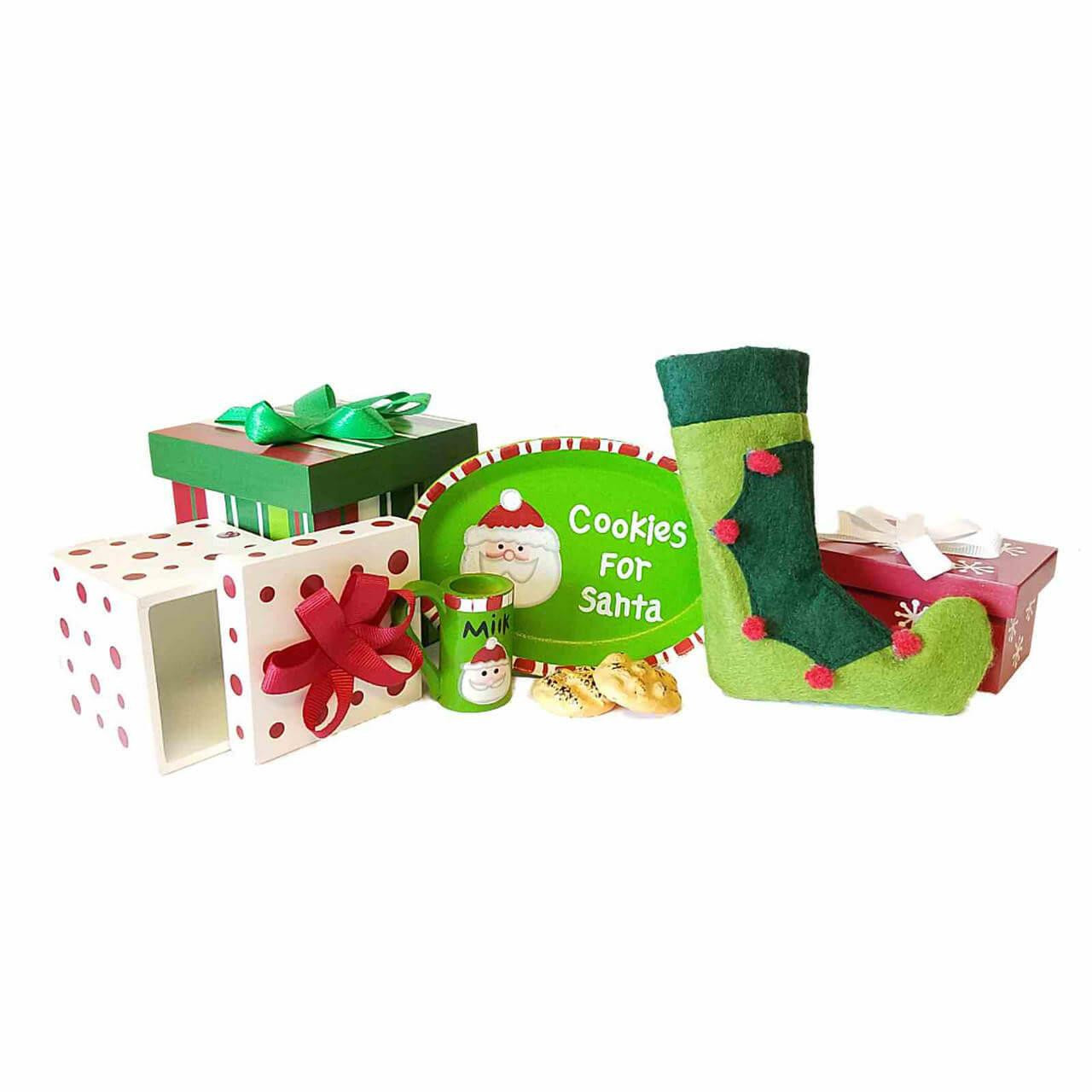 A miniature holiday accessory set is arranged in a cluster against a solid white background. The collection includes a white gift box with red polka dots and a red bow shown half-open, a green striped square gift box with a green bow, and a small red gift box with a white ribbon. In the center, a green oval plate reading "Cookies for Santa" stands upright next to two toy cookies, a tiny green mug labeled "MILK", and a curved green elf stocking with red pom-poms.