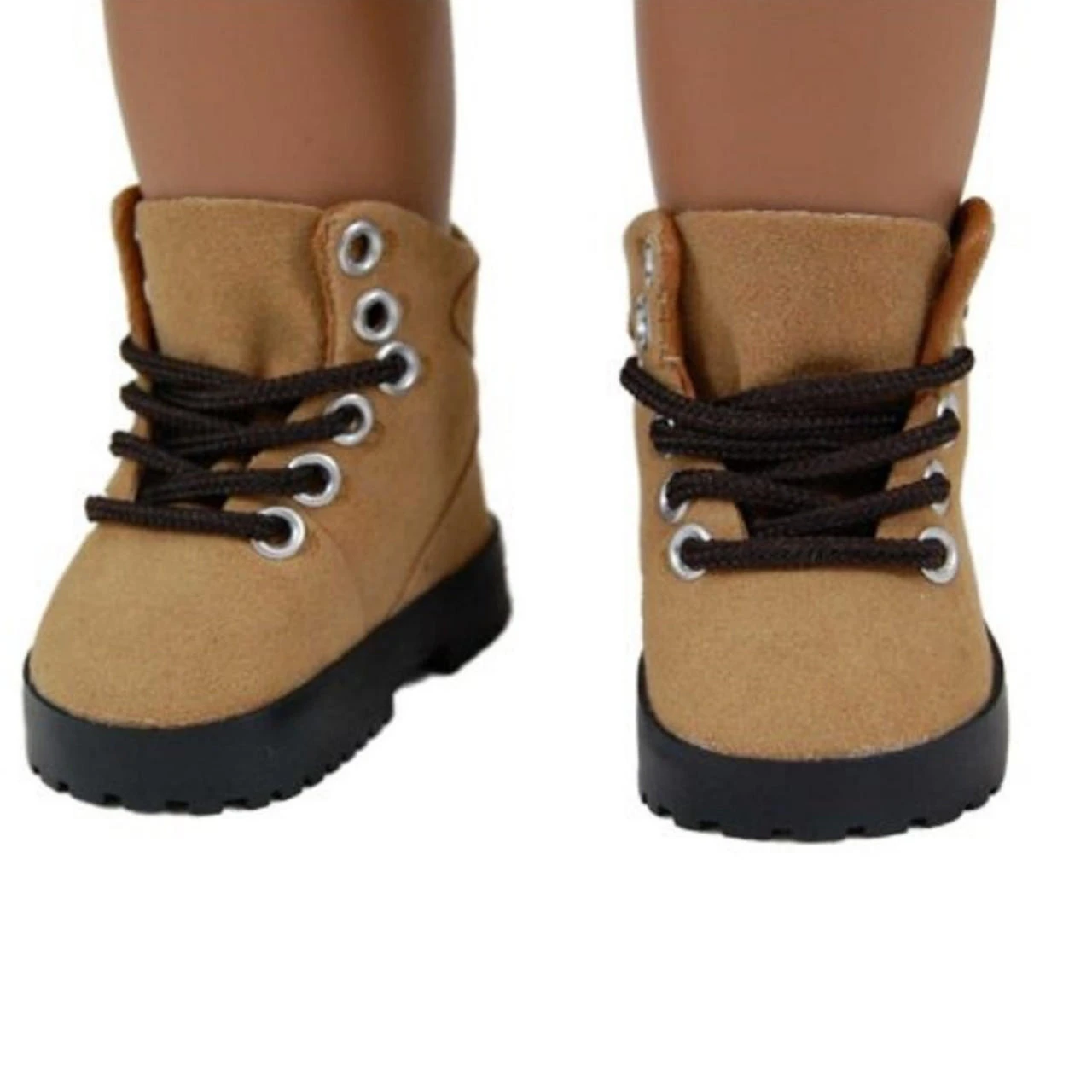 A close-up view shows a doll's feet wearing a pair of tan suede hiking boots by The Queen's Treasures that fits 18in American Girl Dolls. The ankle-high boots feature thick dark brown laces woven through prominent silver metal grommets, paired with heavy, black rugged rubber outsoles against a solid white background.