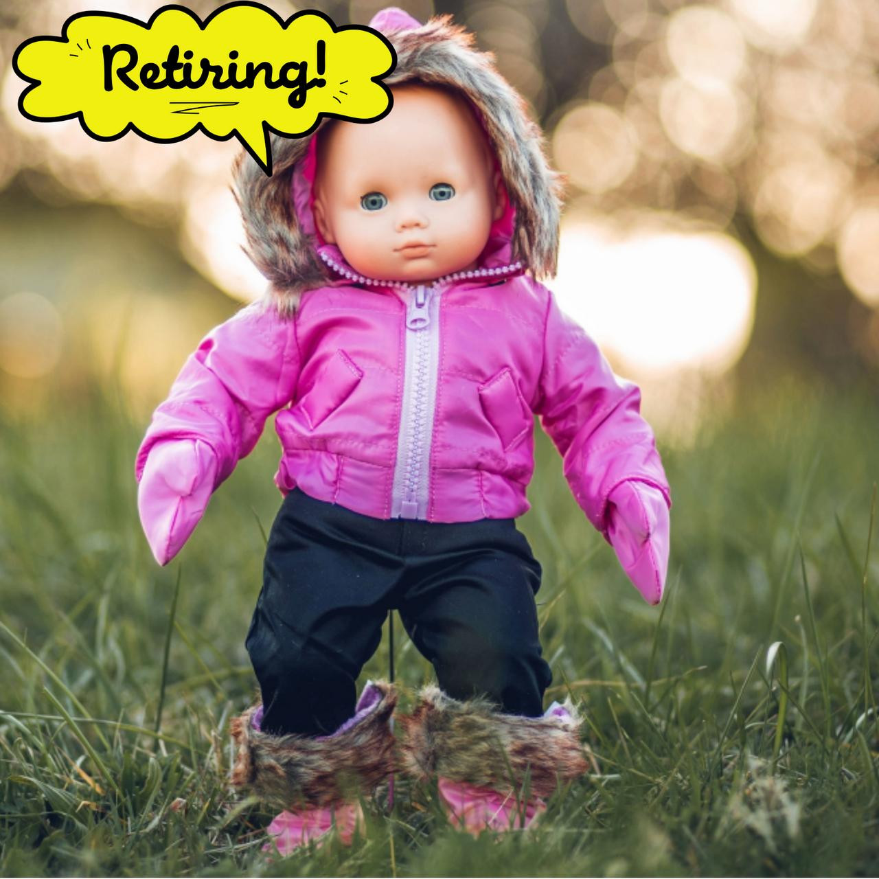 A baby doll stands outdoors in green grass wearing a bright pink hooded winter coat with faux fur trim, dark pants, and matching pink mittens that fits 15" dolls by The Queen's Treasures®. A bright yellow comic book-style speech bubble in the upper left corner reads "Retiring!".