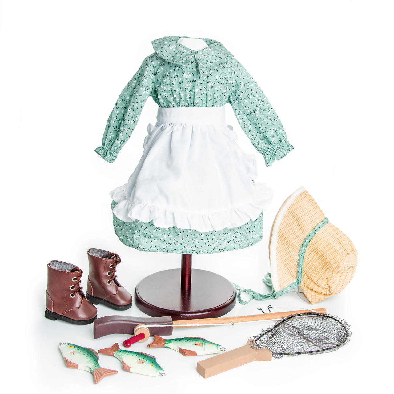 A green pioneer dress on a display stand shown with a matching white apron, bonnet, brown lace-up boots, and miniature fishing accessories on a white background.
