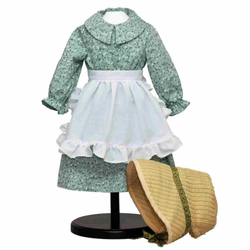 A green calico pioneer dress on a display stand shown with a matching white ruffled apron and a fabric bonnet on a white background.