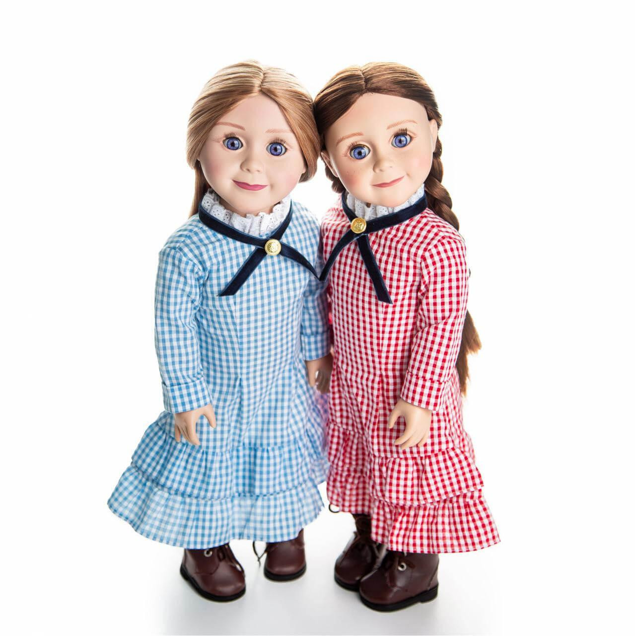 Two 18-inch pioneer dolls stand side-by-side against a plain white background, wearing matching checkered dresses with high lace collars and dark brown boots—one in light blue and the other in red.