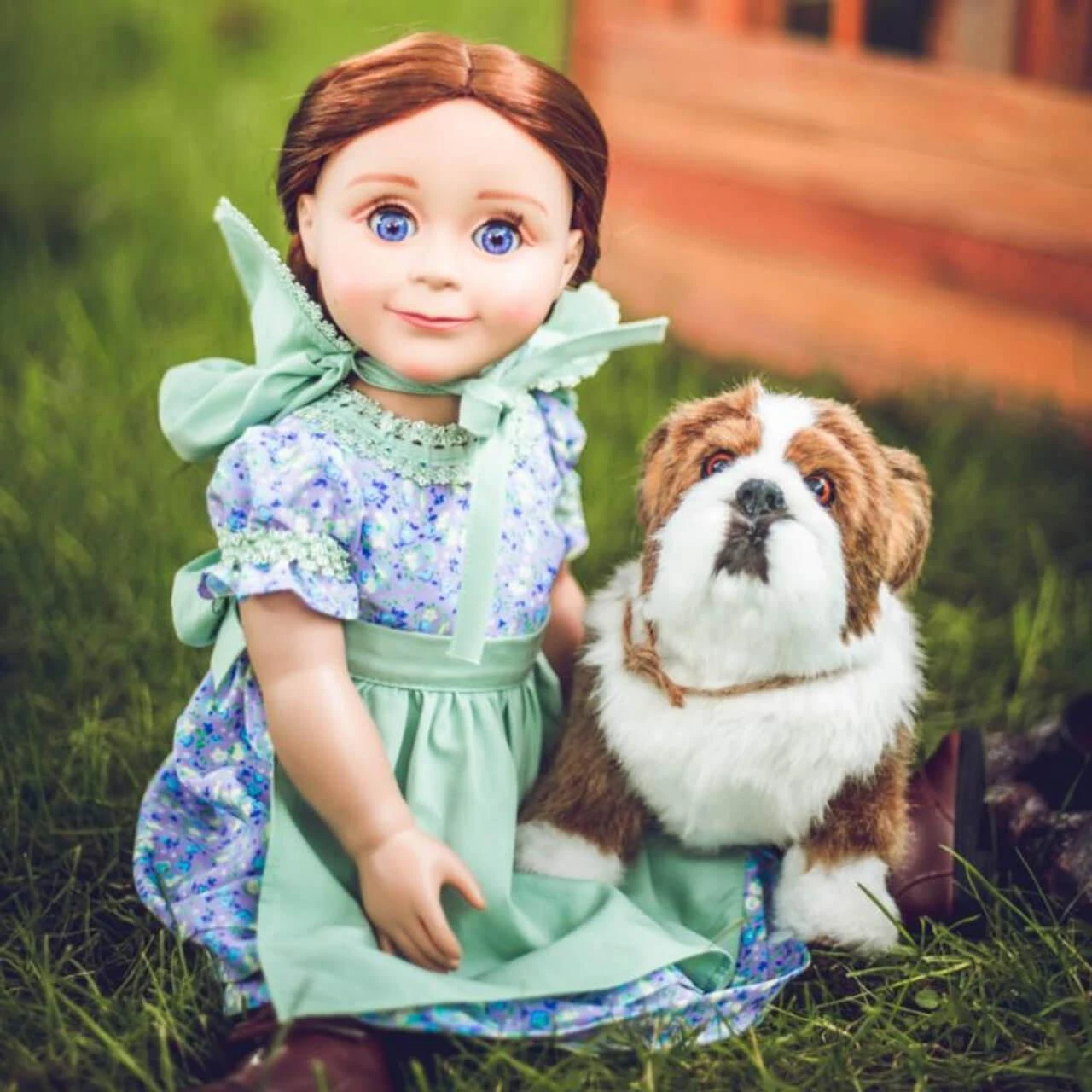 An 18-inch pioneer doll with blue eyes sitting in the grass next to a plush bulldog.