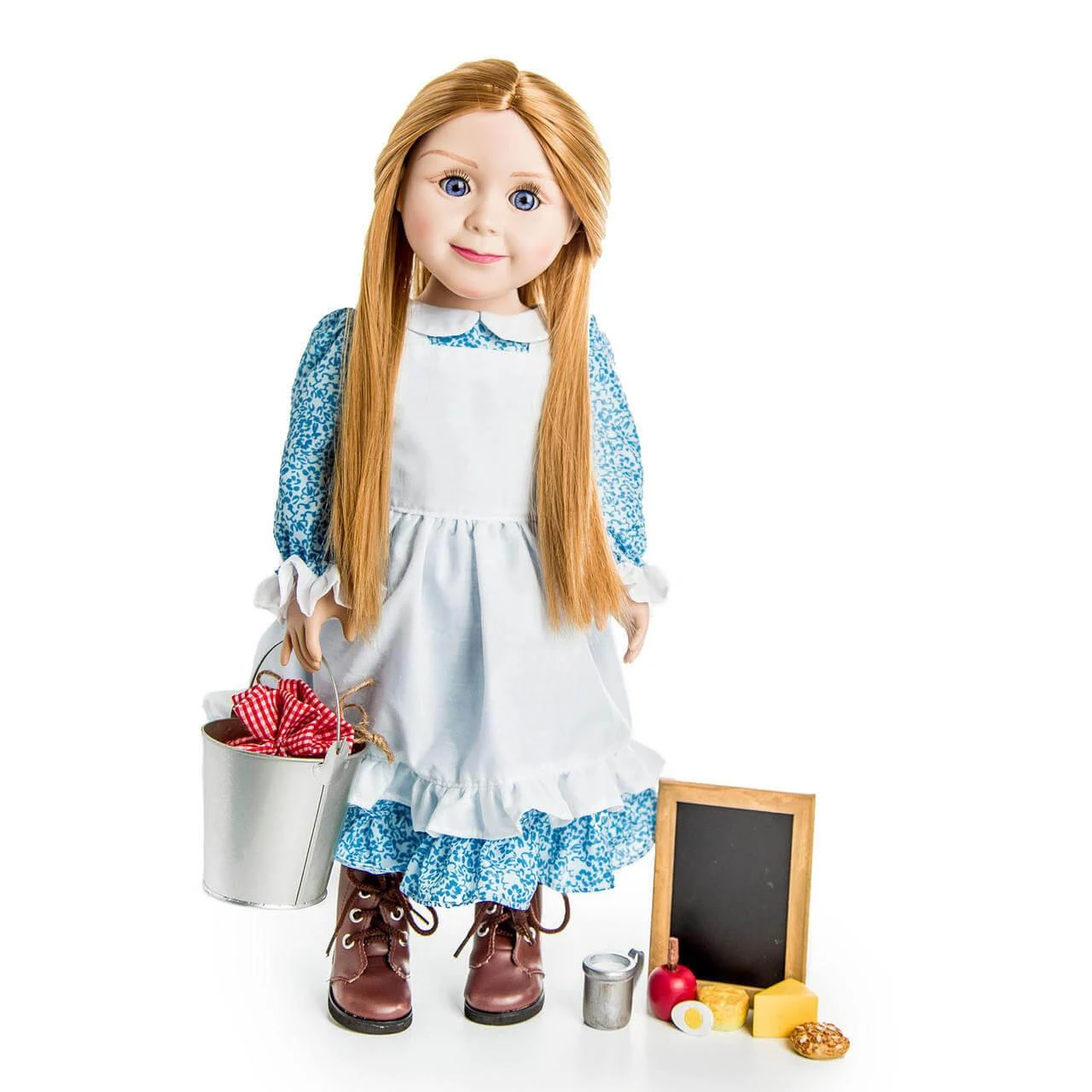 An 18-inch pioneer doll with long blonde hair stands holding a metal bucket, wearing a blue calico dress, white apron, and brown boots, next to miniature school accessories including a small chalkboard and play food.