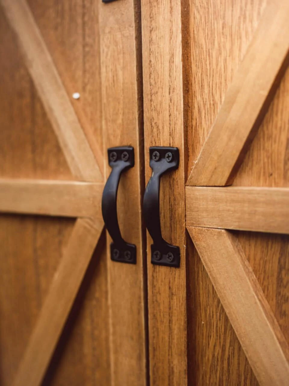 A close-up view of the two black metal handles on the closed sliding barn doors of a wooden doll storage trunk.