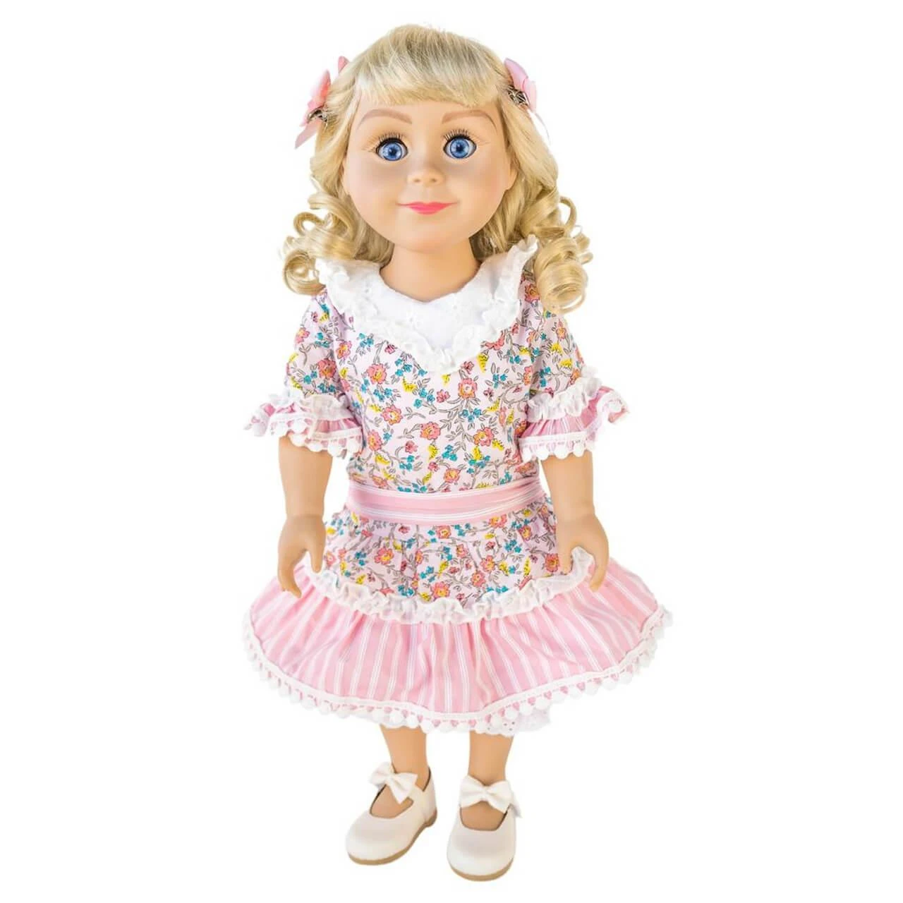 An 18-inch pioneer doll with curly blonde hair standing against a white background, wearing a pink floral calico dress with lace trim and matching pink hair bows.