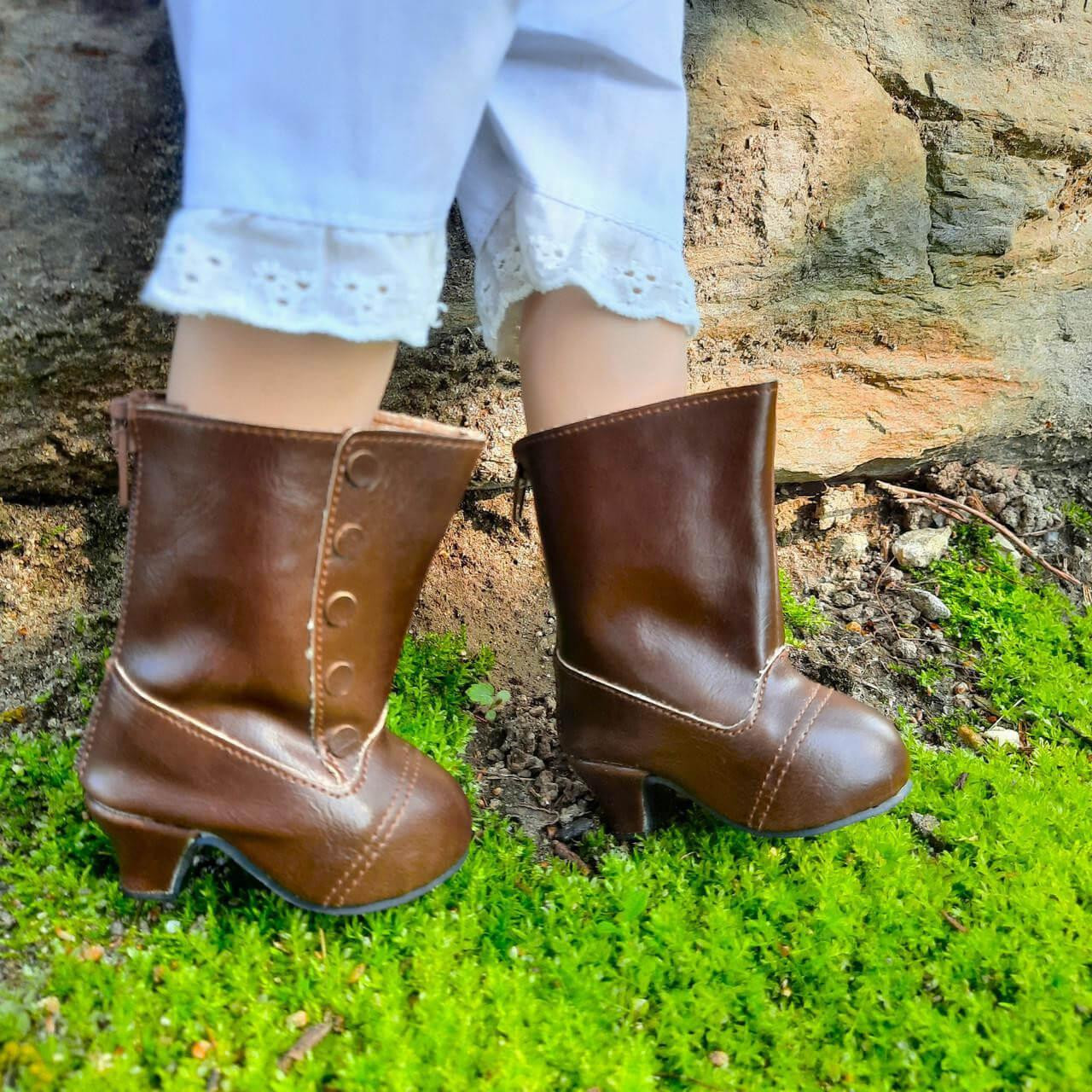 A close-up photograph shows an 18-inch doll wearing brown leather-style boots while standing outdoors.
