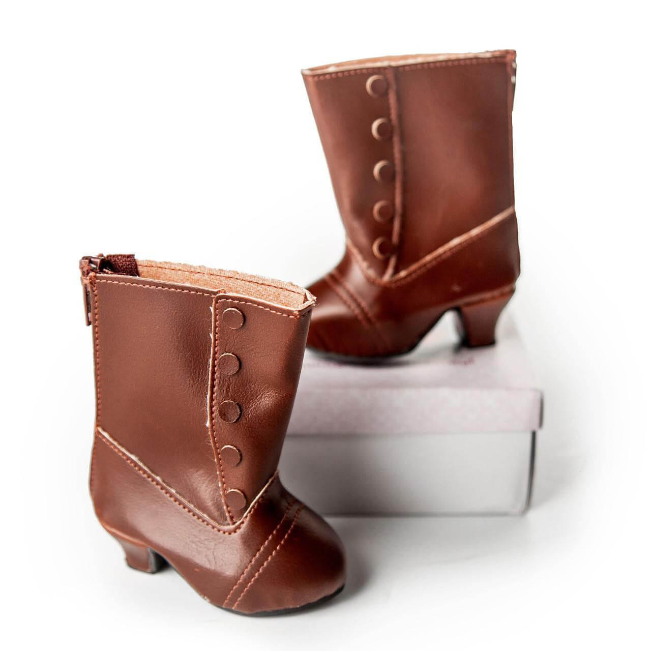 This studio product shot features a pair of realistic miniature brown boots sized for 18-inch dolls, isolated against a seamless white background.