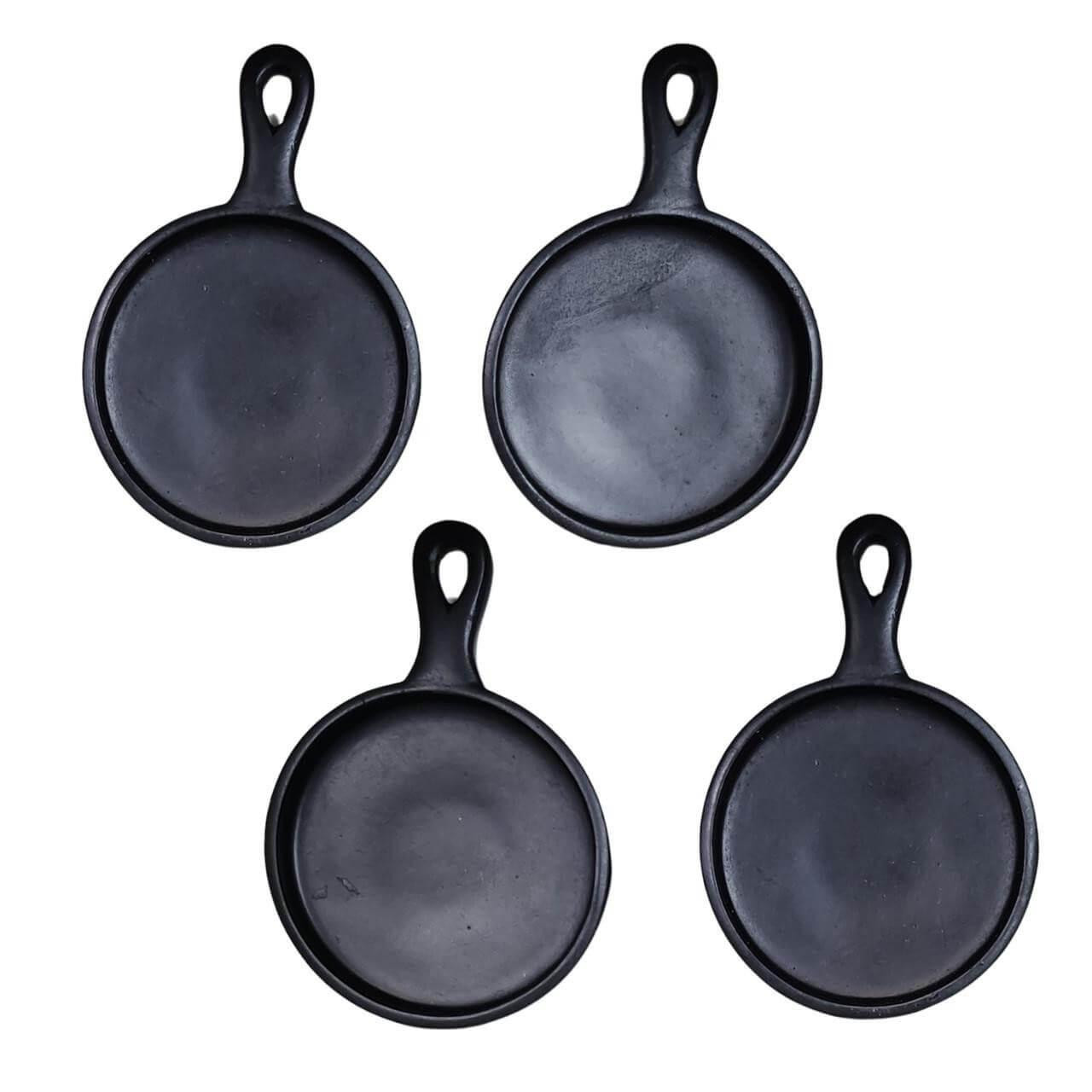 A set of four miniature black cast iron-style frying pans with hanging handles, scaled perfectly to fit 18" American Girl® Dolls, displayed against a solid white background.