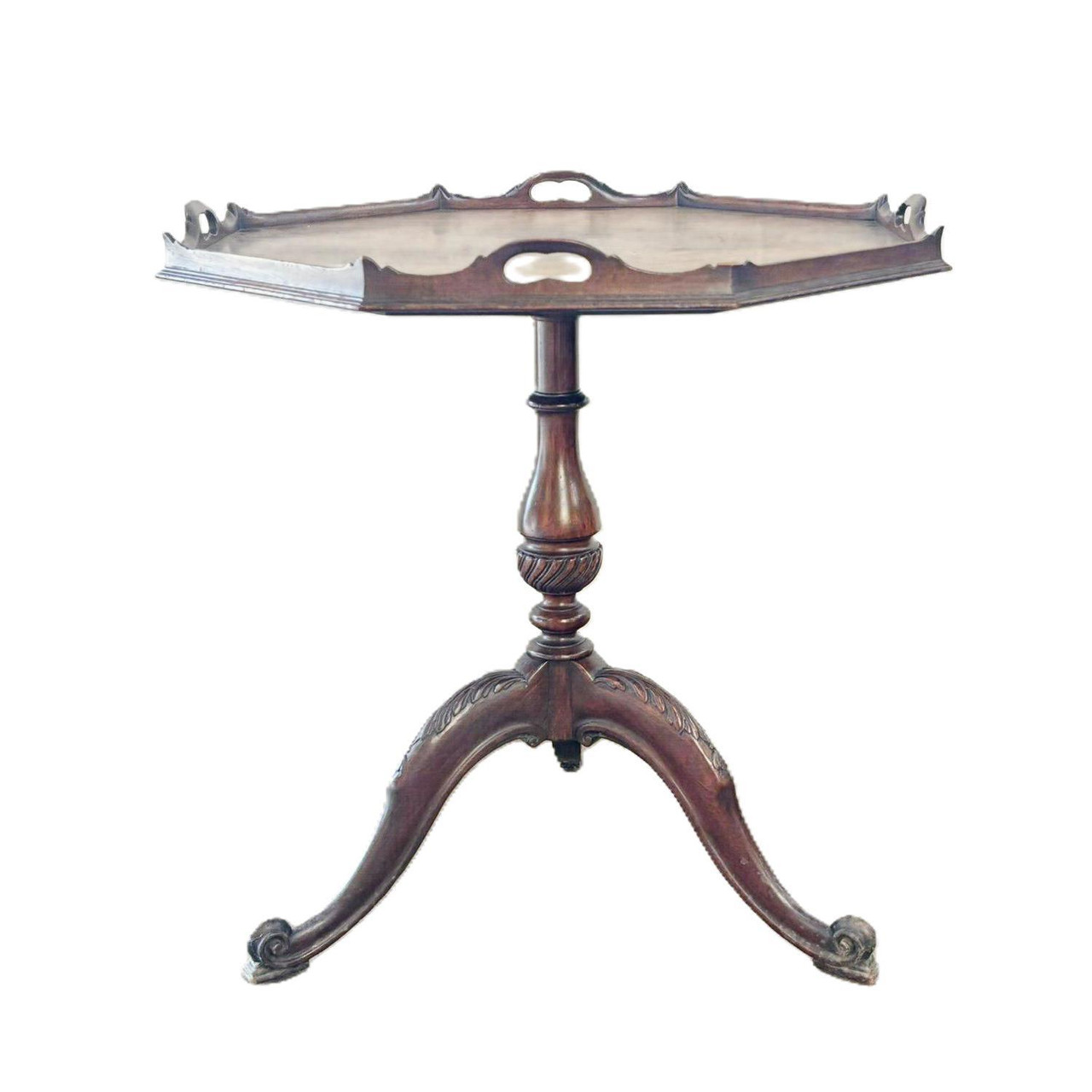 An antique George III style octagonal tripod table crafted from dark mahogany, isolated against a plain white background. The table features an ornate, wavy gallery-top rim with integrated handle cutouts on each side. A single central pedestal column with a spiral-fluted turn connects the top to a three-legged base featuring detailed leaf carvings and elegant scroll feet.