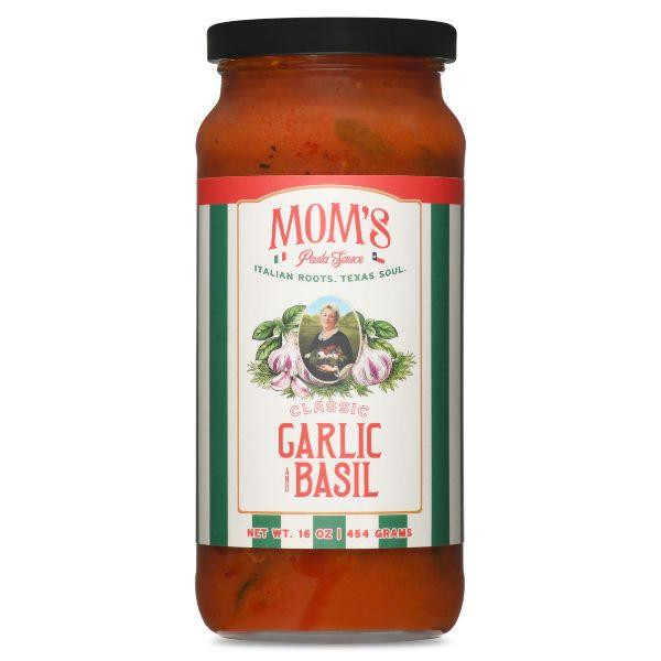 A studio product shot of a 16 oz jar of Mom's Classic Garlic and Basil Pasta Sauce against a solid white background. The jar has a black lid and features a vertical green-and-white striped label framing an illustration of a woman surrounded by garlic cloves and basil leaves.