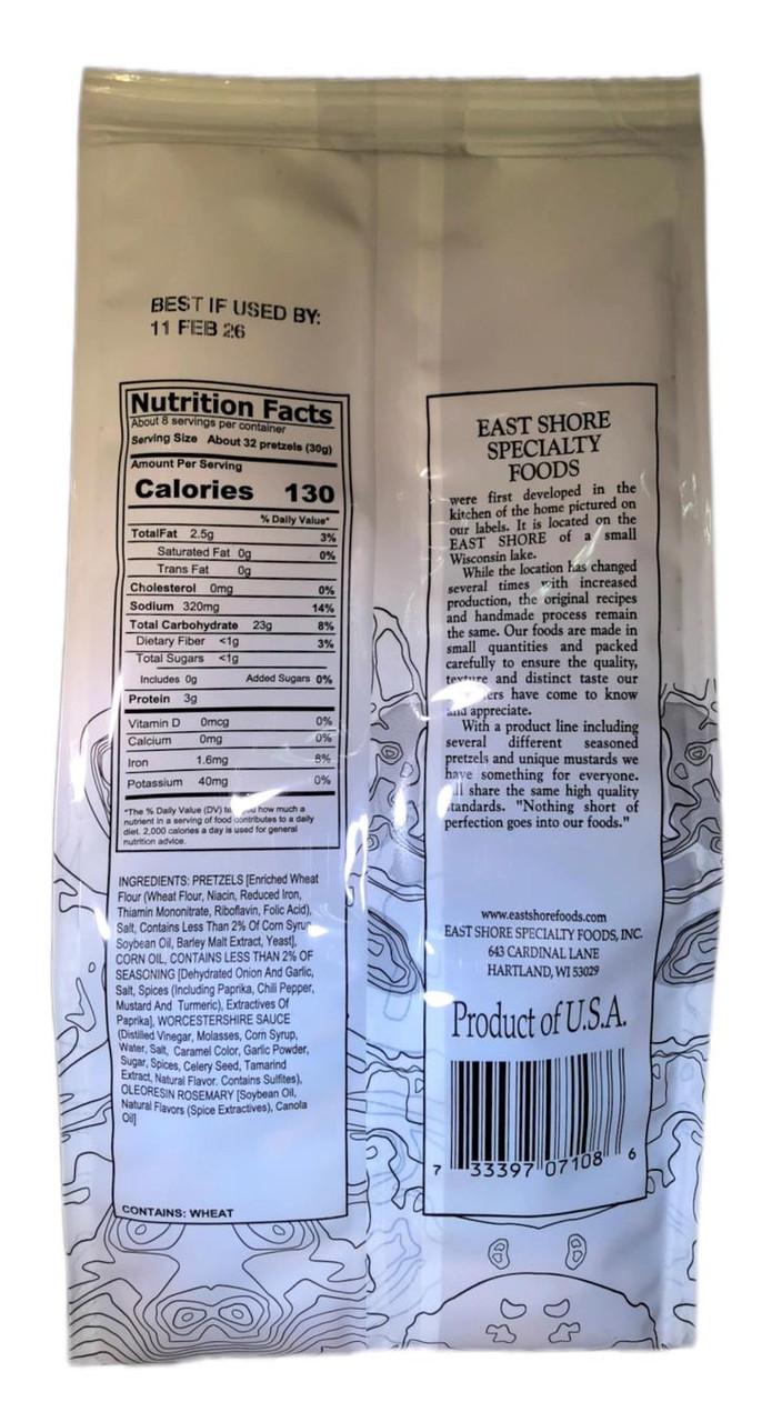 A back-of-pack view of a white East Shore Specialty Foods seasoned pretzels bag displaying its product information. The left column shows the Nutrition Facts panel detailing a 130-calorie serving size, followed by the Ingredients list highlighting enriched wheat flour and savory seasonings, with a clear allergy warning stating "CONTAINS: WHEAT" at the bottom. The right column features a brand heritage story block about East Shore Specialty Foods, their website, a "Product of U.S.A." stamp, and a barcode.