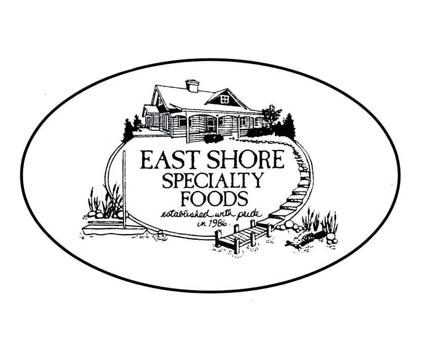 An oval-shaped black and white logo for East Shore Specialty Foods. The center features an illustration of a lakeside country house or cabin situated above a sign that reads "EAST SHORE SPECIALTY FOODS established with pride in 1986." A small wooden dock extends into the water in the foreground, flanked by reeds and stones.