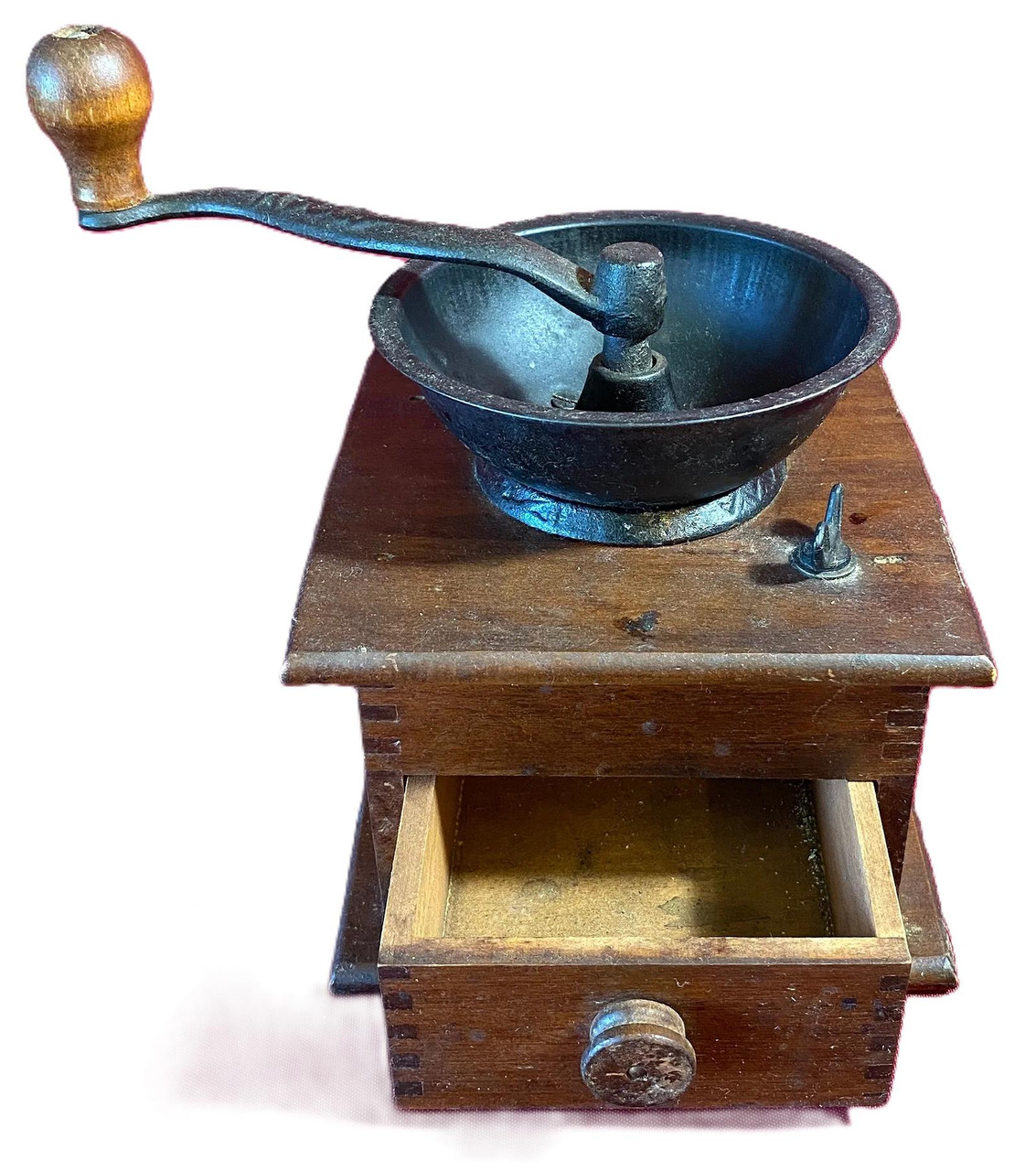 An antique wooden box coffee grinder with a dark cast iron hopper, a hand crank with a wooden knob, and a small drawer pulled open to show its clean interior.
