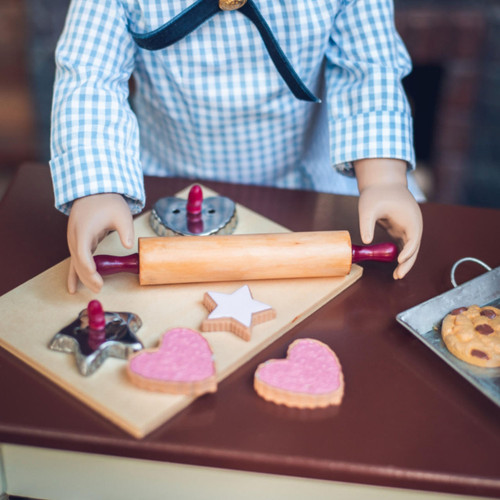 In 18 inch doll kitchen on farmhouse table, a doll holds the rolling pin over a wooden breadboard, with the 2 cookie cutters and 4 star and heart shaped sugar cookies. In 18 inch doll kitchen on farmhouse table, a doll holds the rolling pin over a wooden breadboard, with the 2 cookie cutters and 4 star and heart shaped sugar cookies.