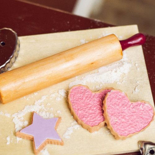 On an 18 inch doll kitchen table 3 of the cookies are on top of a wooden breadboard with a rolling pin next to it.