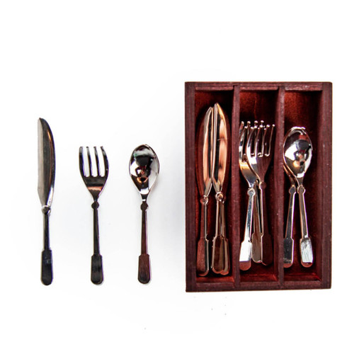 A set of doll-sized silverware is arranged on a solid white background. To the left, a single metal butter knife, fork, and spoon stand vertically in a row. To the right, a rectangular, dark reddish-brown wooden organizer tray holds the rest of the set, with slots neatly separating stacks of matching miniature knives, forks, and spoons.