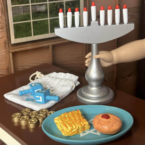 an 18 inch doll holds a candle from the menorah and the  set's 18 inch baked goods on the table. an 18 inch doll holds a candle from the menorah and the  set's 18 inch baked goods on the table.