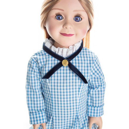 A close-up portrait of a pioneer doll with blue eyes and brown hair wearing a blue and white checkered gingham dress with a blue cross-ribbon collar on a white background.