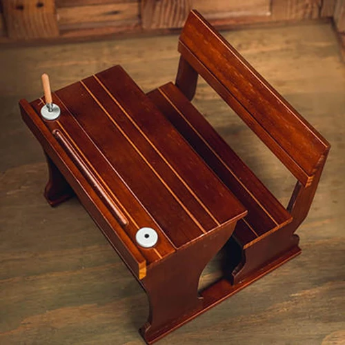 High-angle view of a miniature wooden pioneer school desk with an attached bench on a wood floor.