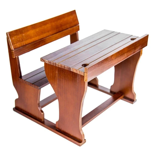 A miniature wooden pioneer school desk with an attached front bench, pencil slots, and inkwell holes against a white background.