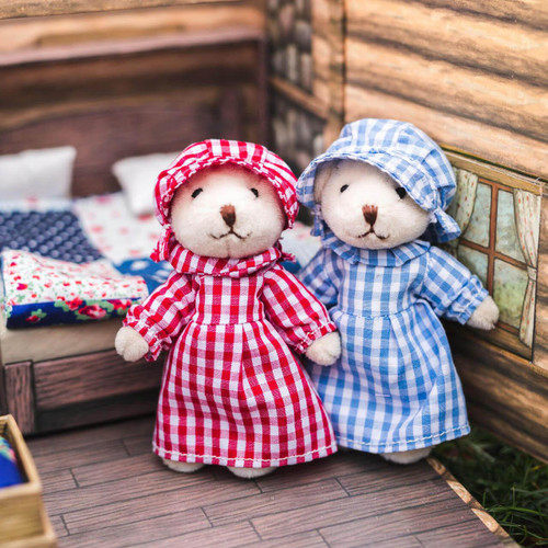Laura and Mary Ingalls are dressed in matching checked dresses with bonnets.
