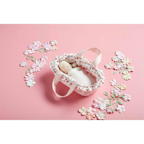 The baby doll with pacifier lays in its bassinet against pink background.