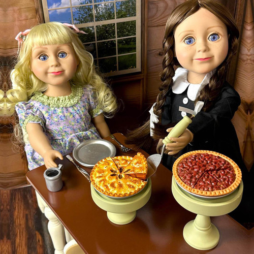In kitchen setting, our 18 inch Nellie Oleson doll sits at the kitchen table with a full place setting and waits for the scullery maid doll to serve her a slice of apple  pie from its pie stand. The pecan pie sits on the taller height pie stand complete. In kitchen setting, our 18 inch Nellie Oleson doll sits at the kitchen table with a full place setting and waits for the scullery maid doll to serve her a slice of apple  pie from its pie stand. The pecan pie sits on the taller height pie stand complete.