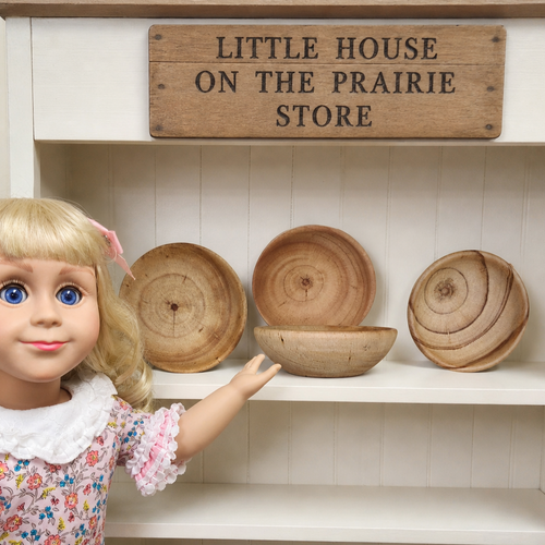 Little House on the Priarie 18 inch doll size store stock shows a set of 4 wooden bowls on a shelf . An 18 inch doll is pointing towards the bowls.
