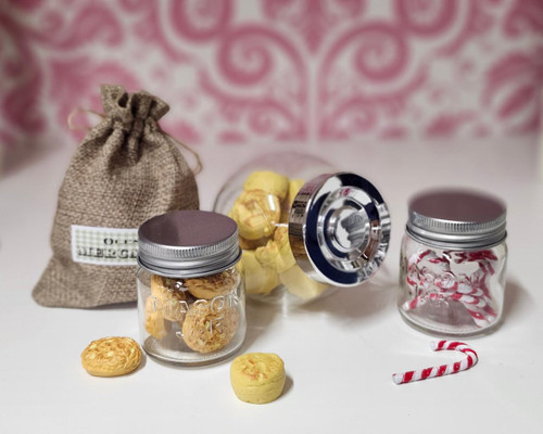 18 inch doll sized slanted jar with biscuits, mason jar with oat cookies and one with candy canes on counter with pink background